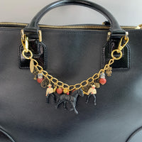 Western bag charm for handbags. Bag chain for handbag with two clasps, two cowboy charms, red beads, bronze charm including a mini bucket, owl, fan, tree and flower with a black horse figurine hanging in the middle. Lenora Dame bag charms.