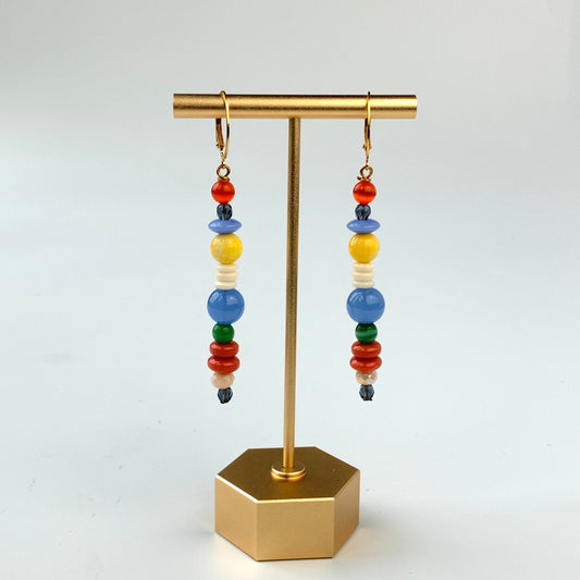 A pair of long skinny earrings with different shaped red, blue, white, and yellow beads. Lenora Dame earrings.