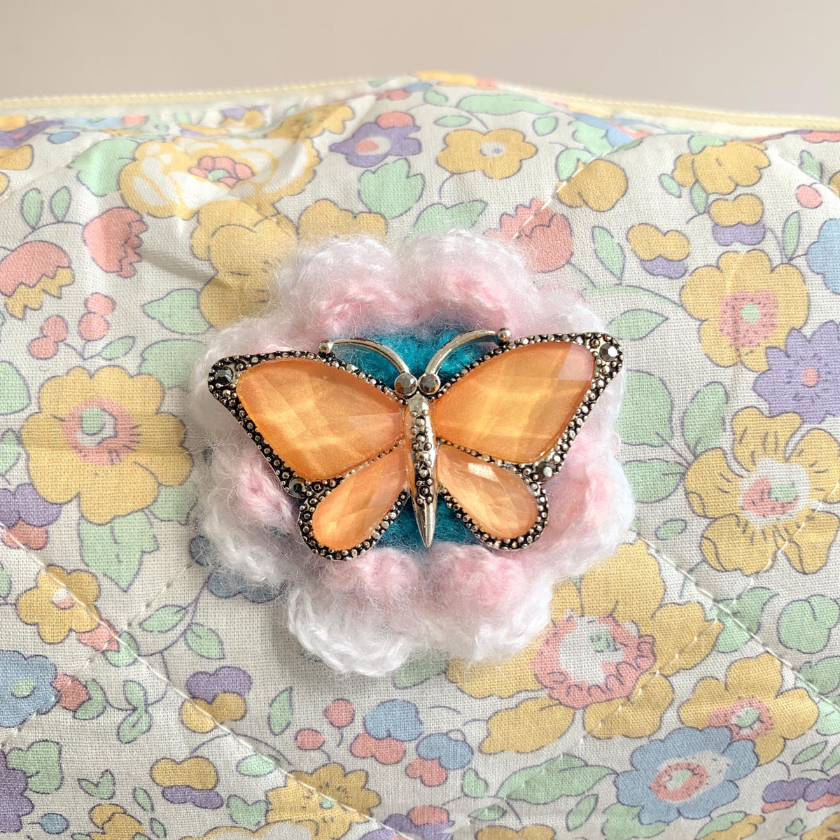 Pastel floral cotton quilted makeup bag embellished with an orange butterfly with rhinestones brooch over a crochet flower. Cute makeup bags with zipper. Bridesmaid gifts for proposal.