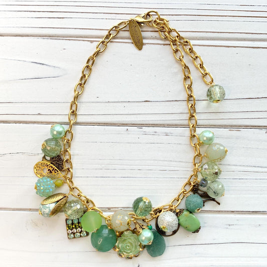 Gold chain charm necklace filled with assorted green beads and charms hanging from a gold cable chain. Lenora Dame necklace. Green statement necklace.