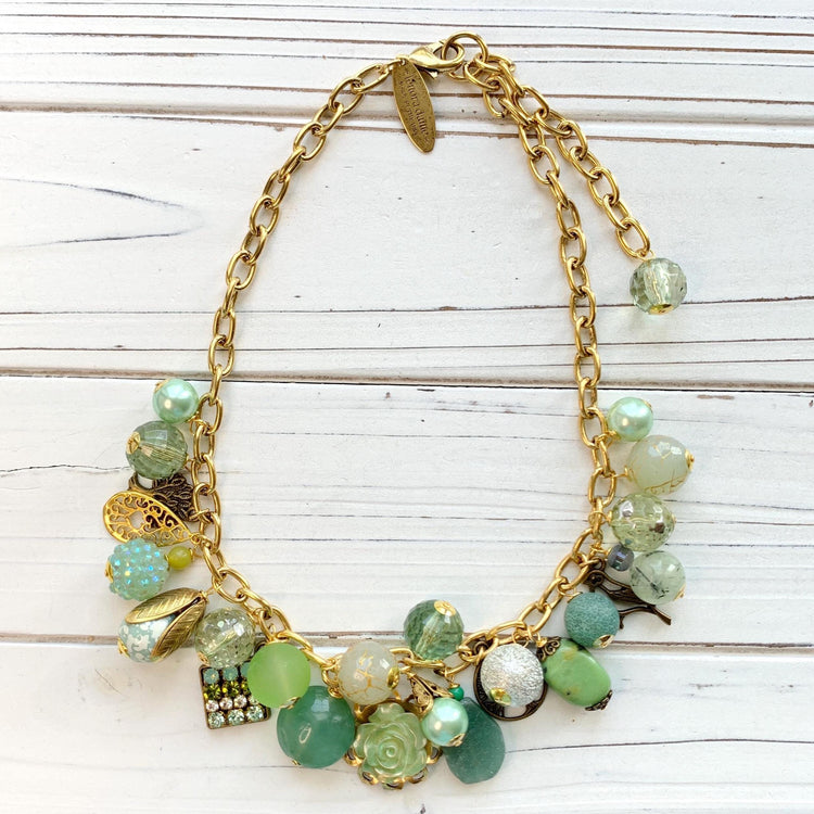 Gold chain charm necklace filled with assorted green beads and charms hanging from a gold cable chain. Lenora Dame necklace. Green statement necklace.