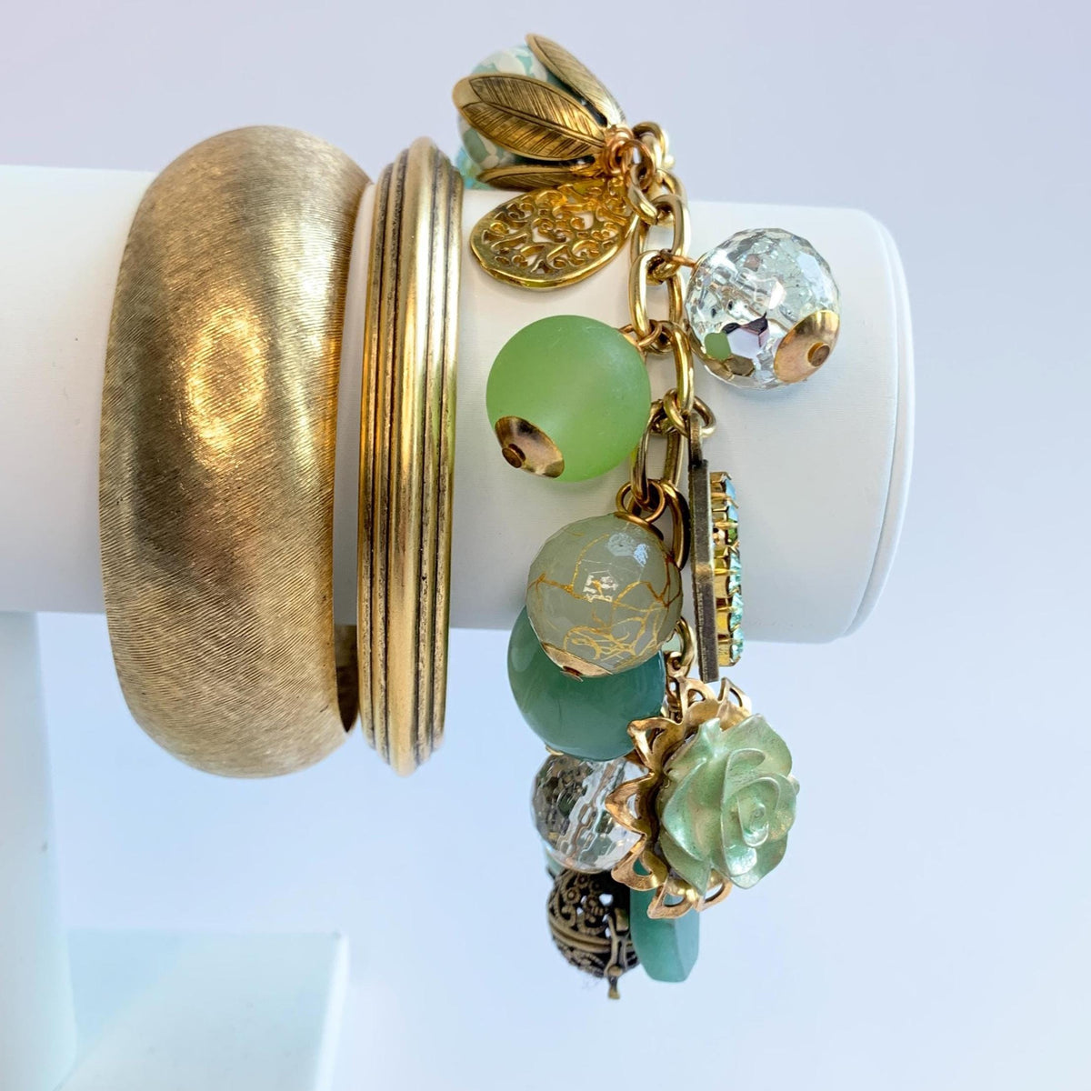 Gold chain charm bracelet filled with assorted green beads and charms hanging from a gold cable chain bracelet. Lenora Dame bracelet. Chunky charm bracelet stack inspiration.