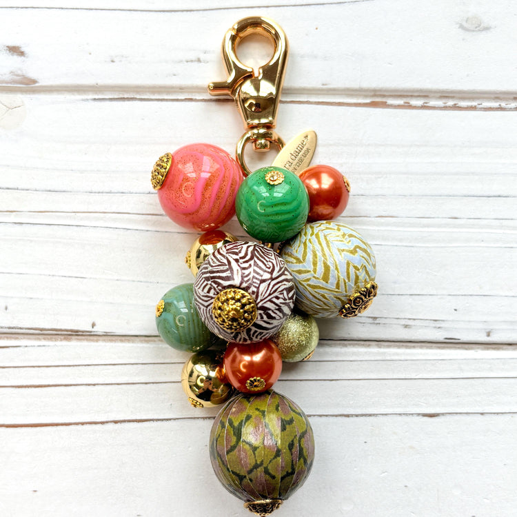 Beaded bag charm with large round beads in a mix of designs in a cluster under a gold trigger clasp. Three beads are wood decoupaged in modern animal prints such as snake print and zebra print. The other beads are gold, rust, green and pink. Lenora Dame bag charm.