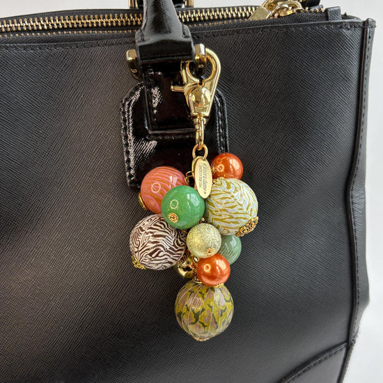 Beaded bag charm with large round beads in a mix of designs in a cluster under a gold trigger clasp. Three beads are wood decoupaged in modern animal prints such as snake print and zebra print. The other beads are gold, rust, green and pink. Lenora Dame bag charm.