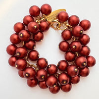 A gold chain bracelet with multiple strands of matte dark red faux pearls. The bracelet has a small tag that reads 'Lenora Dame' and 'Made in the USA.'