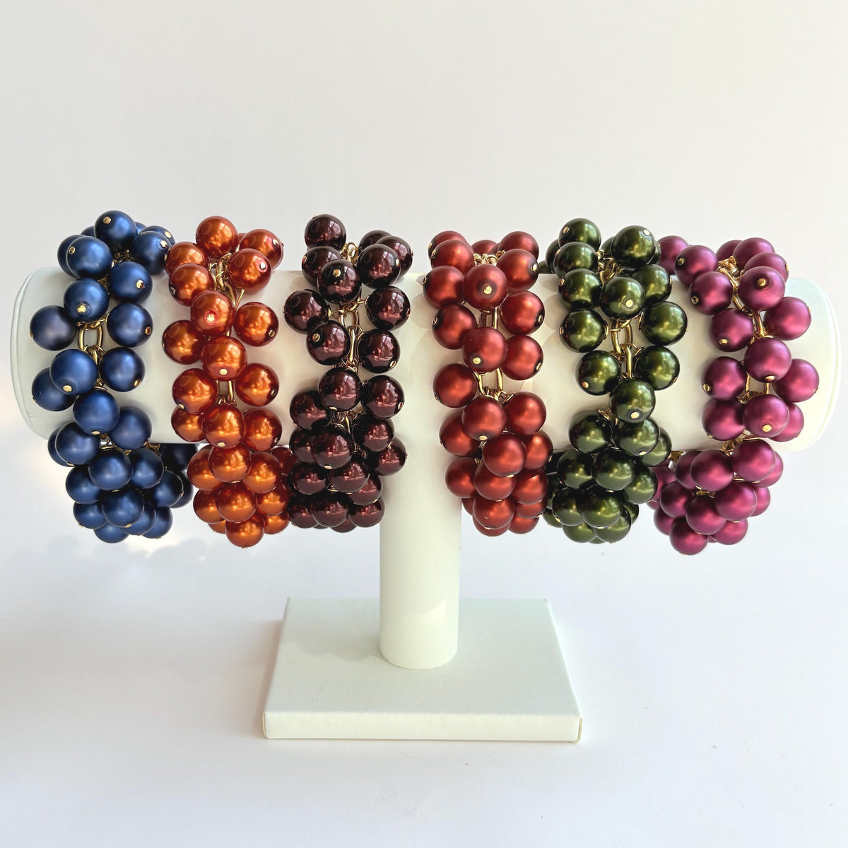 Six colorful pearl bracelets. A navy blue pearl bracelet, a rust colored pearl bracelet, a burgundy pearl bracelet, a hunter green pearl bracelet, and a purple pearl bracelet. Lenora Dame jewelry.