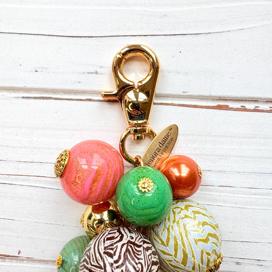 Beaded bag charm with large round beads in a mix of designs in a cluster under a gold trigger clasp. Three beads are wood decoupaged in modern animal prints such as snake print and zebra print. The other beads are gold, rust, green and pink. Lenora Dame bag charm.