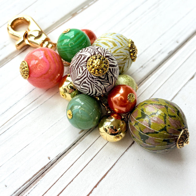 Beaded bag charm with large round beads in a mix of designs in a cluster under a gold trigger clasp. Three beads are wood decoupaged in modern animal prints such as snake print and zebra print. The other beads are gold, rust, green and pink. Lenora Dame bag charm.