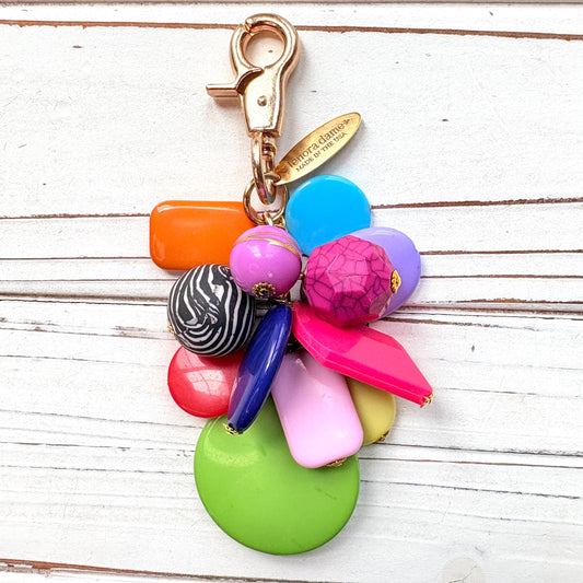 Colorful beaded bag charm with a mix of different shaped beads in a cluster under a gold trigger clasp with a gold oval charm that says Lenora Dame Made in USA. One round black and white zebra bead is among the beads. Lenora Dame bag charm.