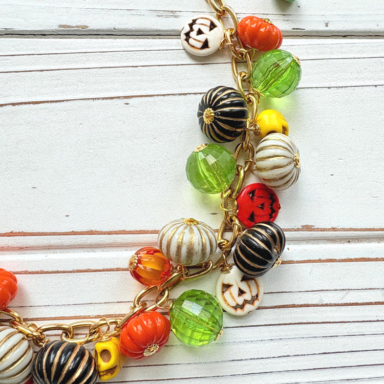Lenora Dame necklace with a gold chain filled with orange and white jack o lantern beads, orange pumpkins, yellow sugar skull beads, black pumpkins, and green beads. Cute necklace for fall.