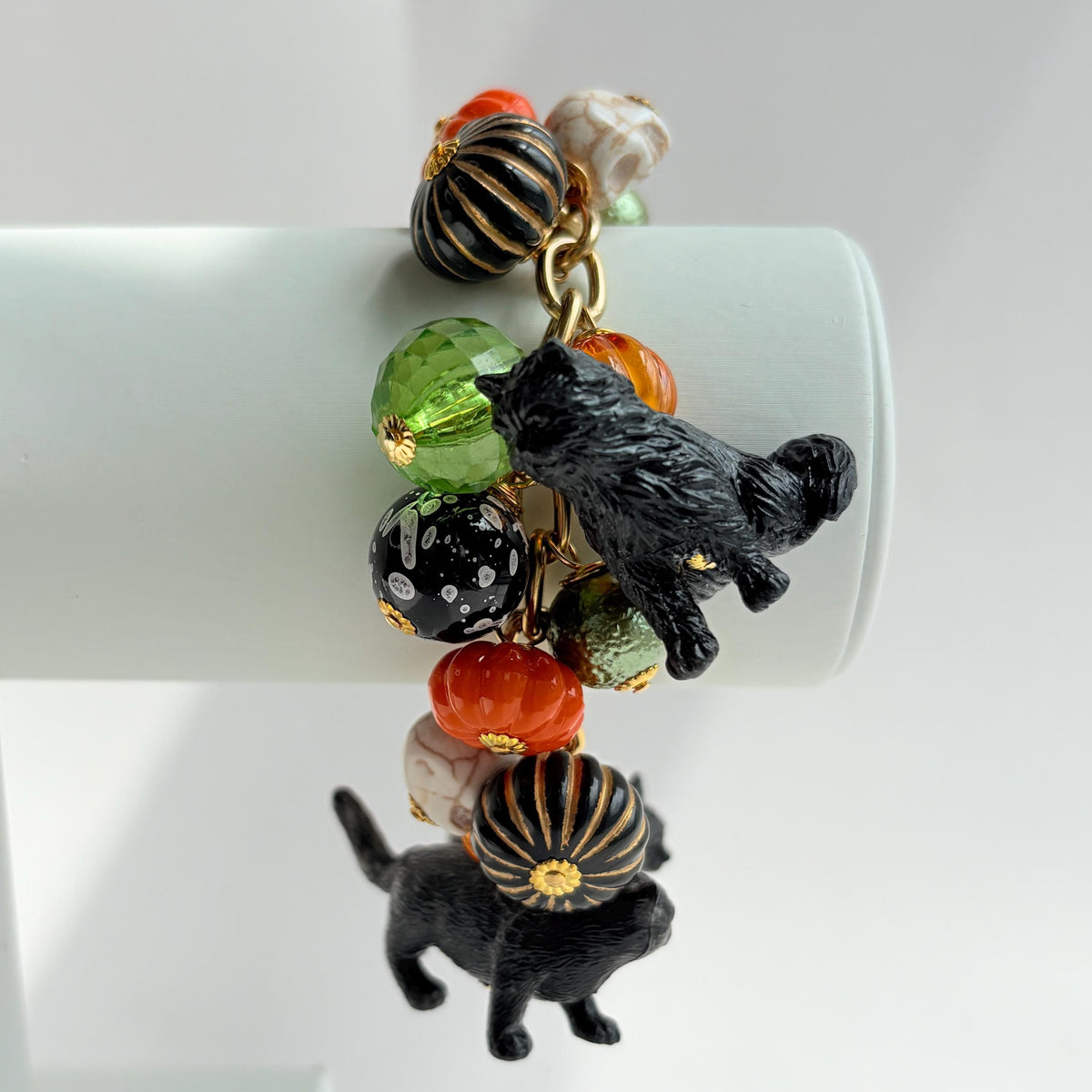 A gold chain bracelet with black cat charms, green and orange beads, and a white pumpkin charm. The bracelet has a tag that reads 'Lenora Dame' and 'Made in USA'.